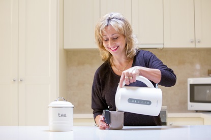 Image shows a woman using an electric kettle in her kitchen.